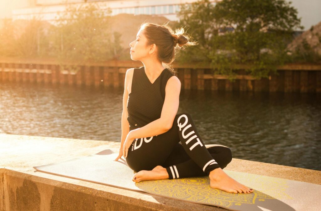 Frau, Die Schwarzes Fitness Outfit Trägt, Führt Yoga In Der Nähe Des Gewässers Durch